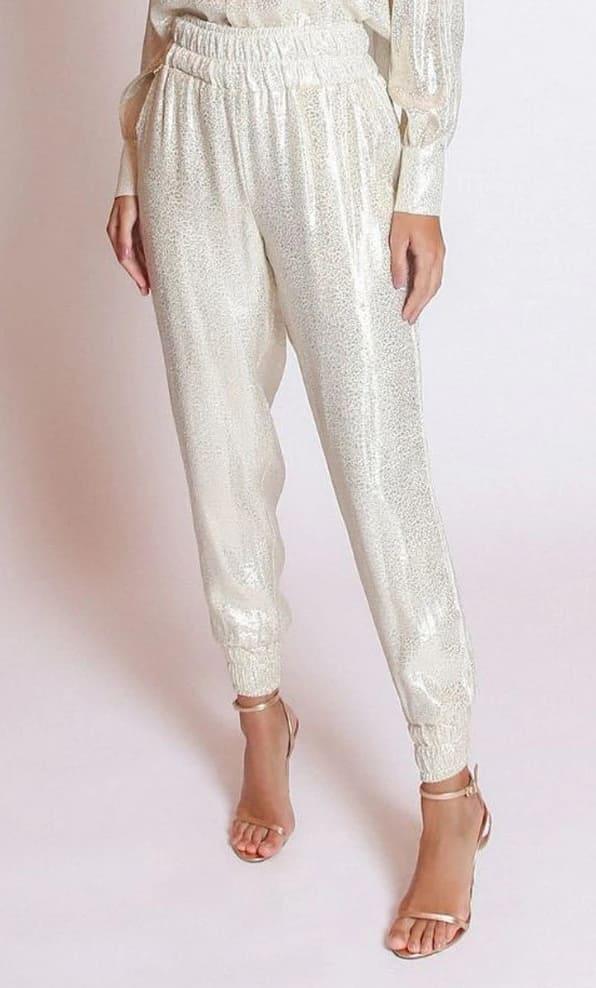 The LETHICIA BRONSTEIN Bibiana Foil Pajama Pants with Lace in off-white gleam under the light. Paired with strappy high-heeled sandals against a white backdrop, they complete a chic look with effortless elegance.